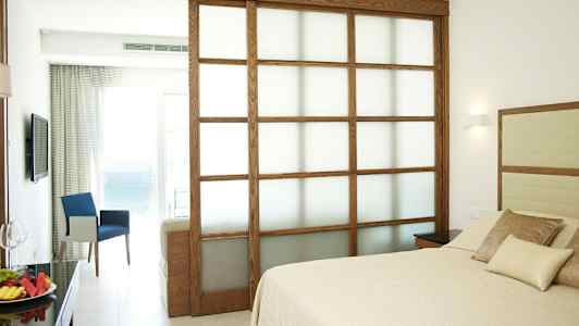 Hotellrom med seng og sittegruppe samt utsikt mot havet. (AI-generert tekst)