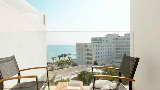 To stoler med bord på balkong med utsikt mot hotellbygninger, palmer og hav. (AI-generert tekst)