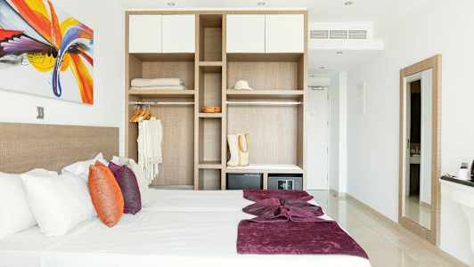 Moderne innredet hotellrom med seng, fargerike puter og åpen garderobe. (AI-generert tekst)