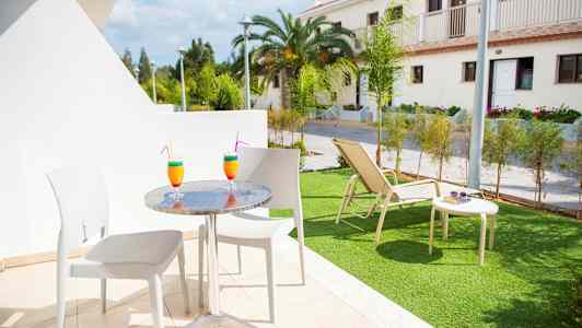 Utemøbler på en terrasse med to fargerike drinker, og en gressplen med solseng i bakgrunnen. (AI-generert tekst)