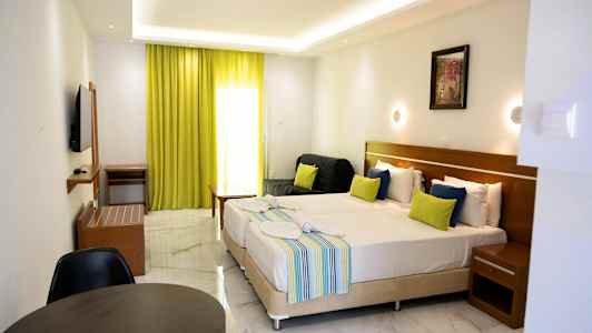 Et hotellrom med to oppredde senger, fargerike puter, en liten sittegruppe og limegrønne gardiner. (AI-generert tekst)