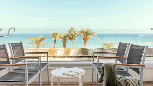 Utsikt fra en terrasse med stoler, bord og havet i bakgrunnen. (AI-generert tekst)