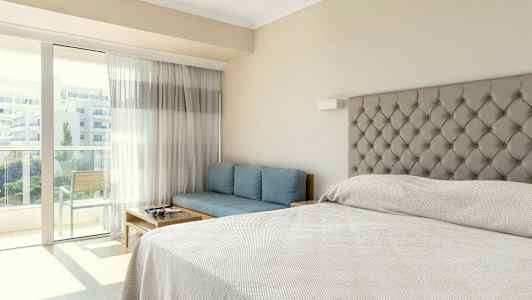 Et hotellrom med en seng, en blå sofa og en balkong. (AI-generert tekst)