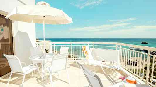 En solrik terrasse med utsikt over havet, stoler og parasoll. (AI-generert tekst)