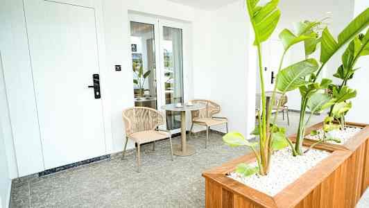 En uteplass med to stoler og et bord, omgitt av grønne planter. (AI-generert tekst)