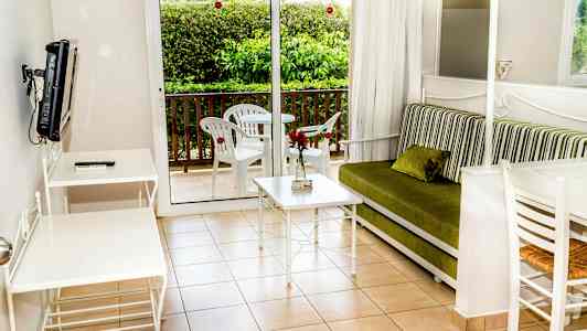 En stue med en grønn sofa, hvitt bord og stoler, samt en balkong med utemøbler. (AI-generert tekst)