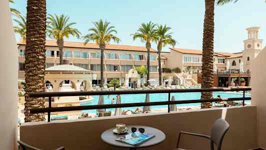 Utsikt fra en balkong mot et basseng og omkringliggende hotellbygninger. (AI-generert tekst)