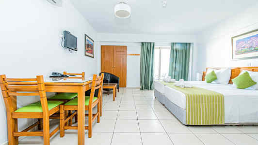 Et hotellrom med en seng, et spisebord med stoler og en veggmontert TV. (AI-generert tekst)