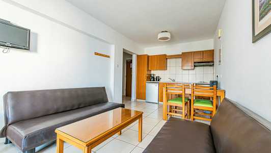 En innendørs med to brune sofaer, et glassbord og en kjøkkenområde med treskap og spiseplass. (AI-generert tekst)