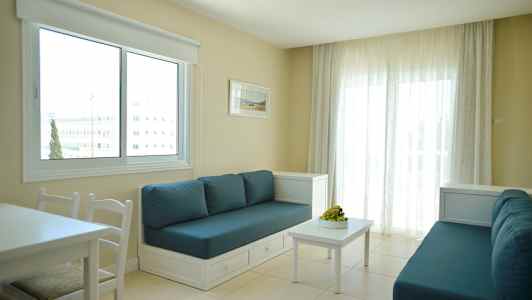 Et rom med to sofaer med blå puter, et hvitt bord og et stort vindu med hvite gardiner. (AI-generert tekst)