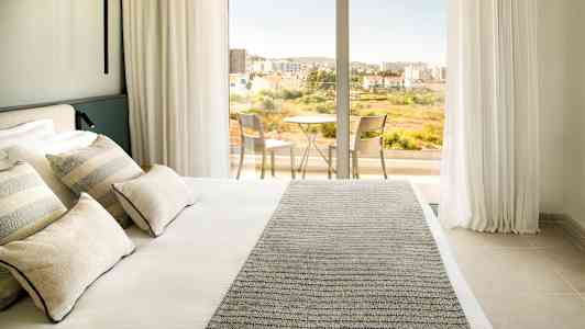 Hotellrom med en dobbeltseng og tilgang til balkong med bord og stoler. (AI-generert tekst)