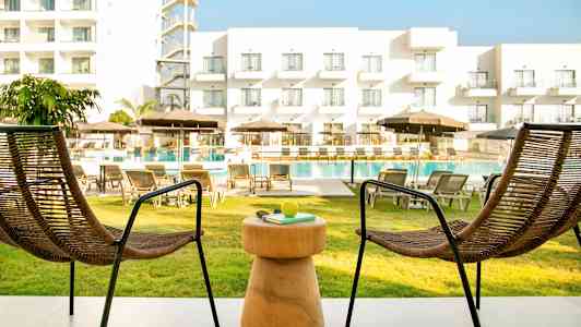 To stoler og et bord på en uteplass med utsikt over bassengområdet og et hotell. (AI-generert tekst)