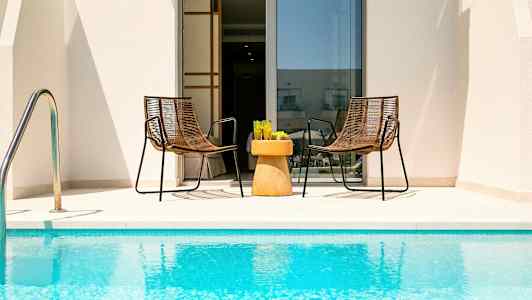 To stoler og et bord med glass står ved bassenget foran en dør. (AI-generert tekst)