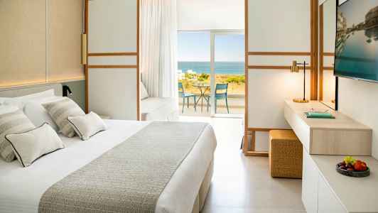 Et hotellrom med en stor seng, TV og utsikt over havet fra en balkong. (AI-generert tekst)