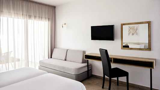 Et hotellrom med to senger, en sofa, et skrivebord og en veggmontert TV. (AI-generert tekst)