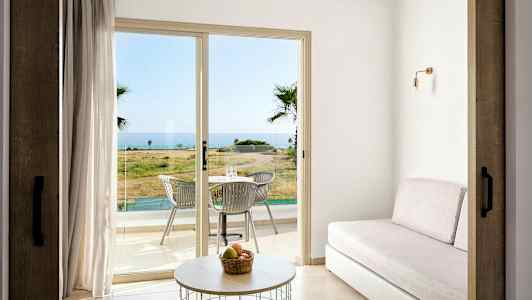 Et rom med sofa, bord og glassdører som fører ut til en terrasse med bord og stoler, med havutsikt. (AI-generert tekst)
