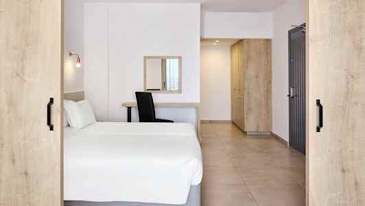 Et hotellrom med en dobbeltseng, skrivebord, speil og oppbevaringsmøbler. (AI-generert tekst)