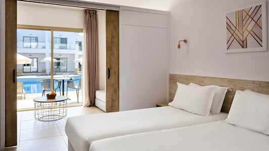 Hotellrom med to enkeltsenger og utsikt mot et utendørs basseng og solsenger. (AI-generert tekst)