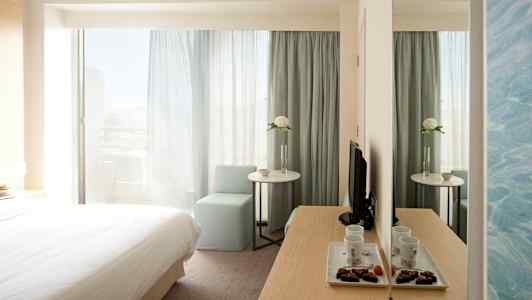 Hotellrom med seng, bord, stol og speil. (AI-generert tekst)