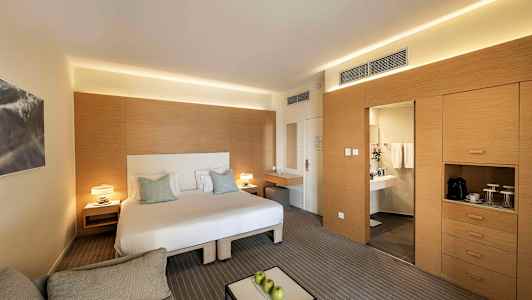 Et moderne hotellrom med en dobbeltseng, en sittegruppe og et skrivebord. Til høyre er det et skap og en dør som fører til et bad. (AI-generert tekst)