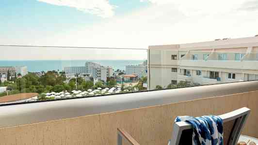 Utsikt fra balkong over hotellområde og hav. (AI-generert tekst)