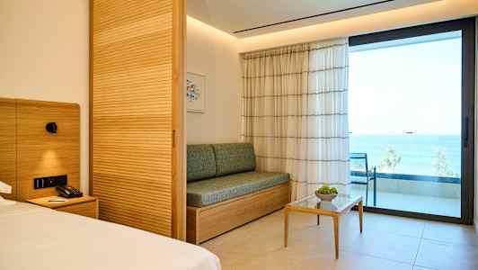 Et hotellrom med moderne innredning, en sofa, et lite bord og en balkong med havutsikt. (AI-generert tekst)