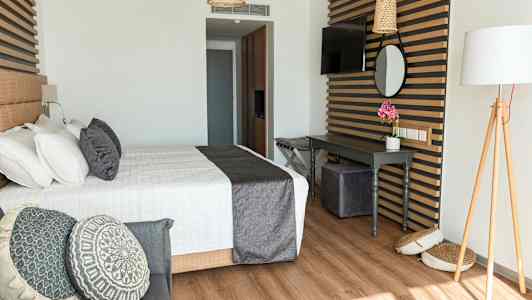 Et stilfullt hotellrom med en seng, dekorative puter og et skrivebord. (AI-generert tekst)