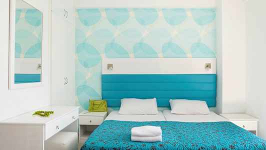 Et hotellrom med to senger, blå trekk og hvit innredning. (AI-generert tekst)