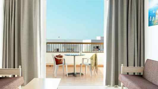 Et hotellrom med utsikt over en balkong med et bord og stoler. (AI-generert tekst)