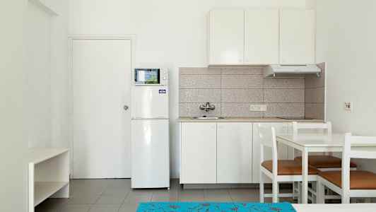 Et kjøkken med hvit innredning, inkludert kjøleskap, mikrobølgeovn og spisebord med stoler. (AI-generert tekst)