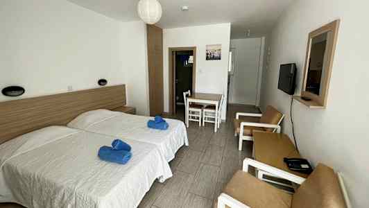 Hotellrom med to enkeltsenger, bord med stoler og en sofagruppe. (AI-generert tekst)