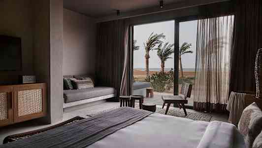 Et hotellrom med en seng og utsikt over palmer utenfor et glassvindu. (AI-generert tekst)