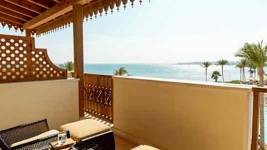 Balkong med kurvmøbler og utsikt over havet og palmer. (AI-generert tekst)