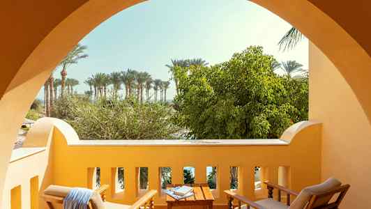 Balkong med sittemøbler foran en utsikt av trær og palmer. (AI-generert tekst)