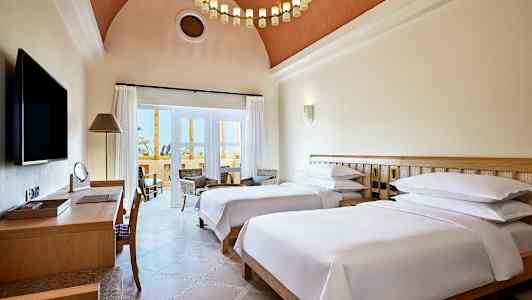 Hotellrom med to enkeltsenger, skrivebord og sittegruppe ved balkongen. (AI-generert tekst)