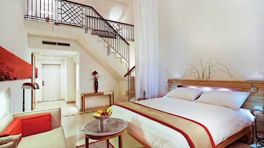 Moderne innredet hotellrom med dobbeltseng, sittegruppe og trapp til loft. (AI-generert tekst)