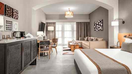 Et hotellrom med en seng, sittegruppe og spisebord, samt moderne interiør. (AI-generert tekst)