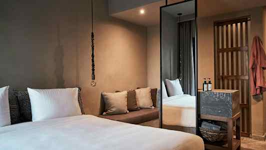 Et soverom med en stor seng, puter, en sofa og et høyt speil. (AI-generert tekst)