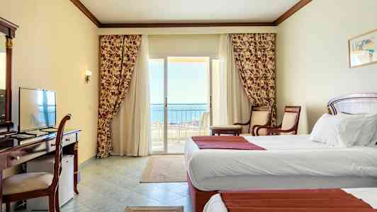 Hotellrom med hvite vegger, to enkeltsenger og en balkong med utsikt over havet. (AI-generert tekst)