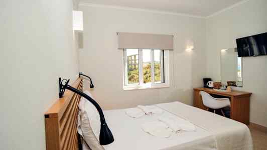 Et hotellrom med en seng, vindu, skrivebord, stol og TV. (AI-generert tekst)