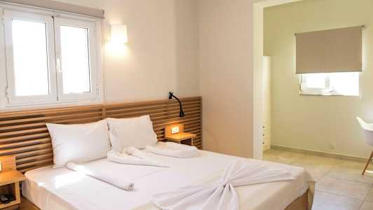 Et hotellrom med en dobbeltseng, trepaneler som sengegavl, og en vinduslampe ovenfor. Et lite bord med en leselampe og en åpning til en annen del av rommet. (AI-generert tekst)