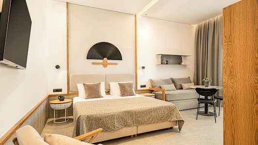 Et stilrent hotellrom med en dobbeltseng, sofa, bord og en veggmontert TV. (AI-generert tekst)