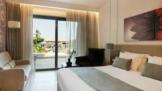 Hotellrom med dobbeltseng og utsikt over uteområdet gjennom en glassdør. (AI-generert tekst)