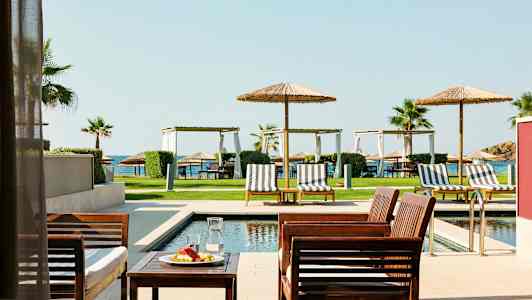 Utendørsmøbler ved et basseng med solsenger og parasoller, plen og hav i bakgrunnen. (AI-generert tekst)