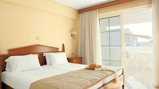 Et hotellrom med en dobbeltseng, lyse gardiner og en balkong med utemøbler. (AI-generert tekst)