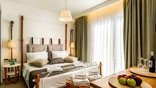 Et hotellrom med en dobbeltseng, sengetøy og pynteputer. To håndklær og et vinsett er plassert på benker ved foten av sengen. (AI-generert tekst)