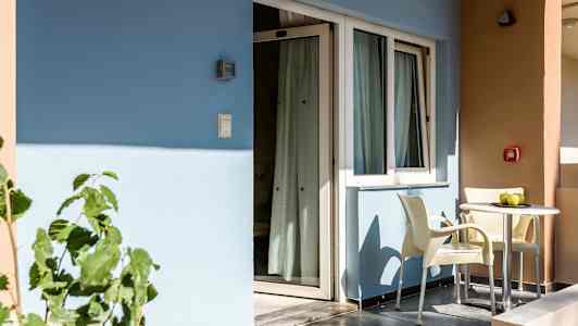 En balkong med to stoler og et bord står foran en bygning med blå og beige vegger. (AI-generert tekst)