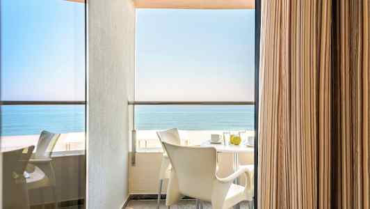 Balkongutsikt med bord og stoler og havet i bakgrunnen. (AI-generert tekst)