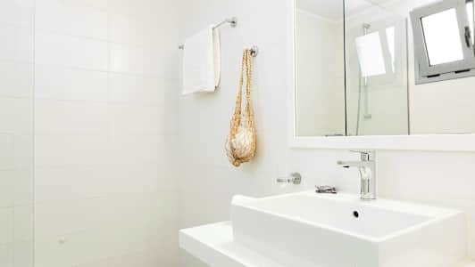 Et lyst baderom med hvite fliser på veggen, vask, håndklehenger og speil. (AI-generert tekst)