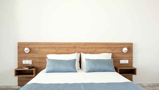 Seng med blått sengeteppe og puter, trebord på hver side. (AI-generert tekst)